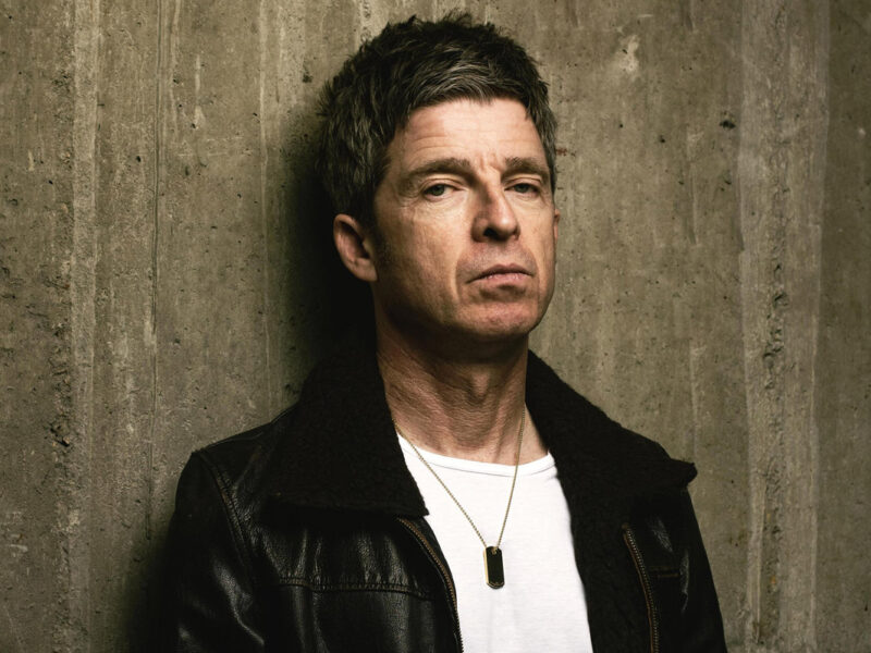 noel gallagher posing wearing a leather jacket