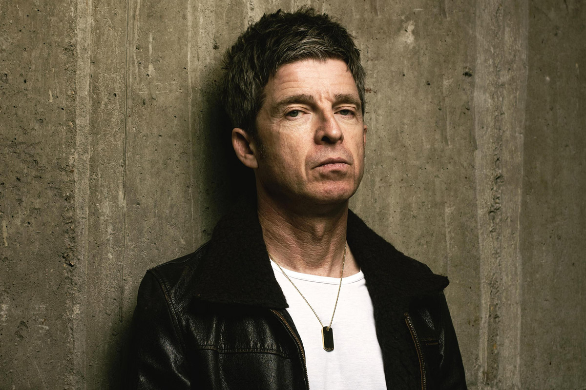 noel gallagher posing wearing a leather jacket